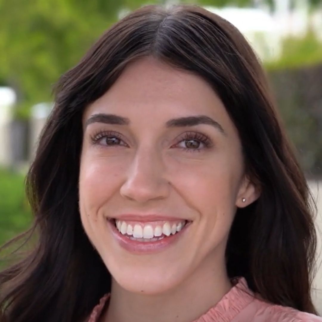Smiling woman with long dark hair outdoors.