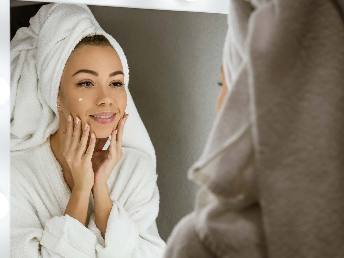 Woman applying cream in front of mirror.