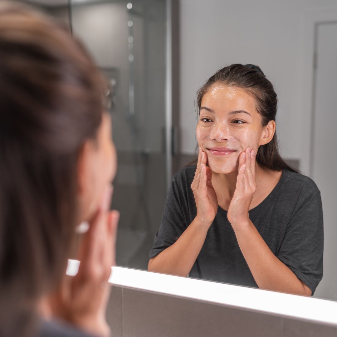 Woman applying face wash in mirror.