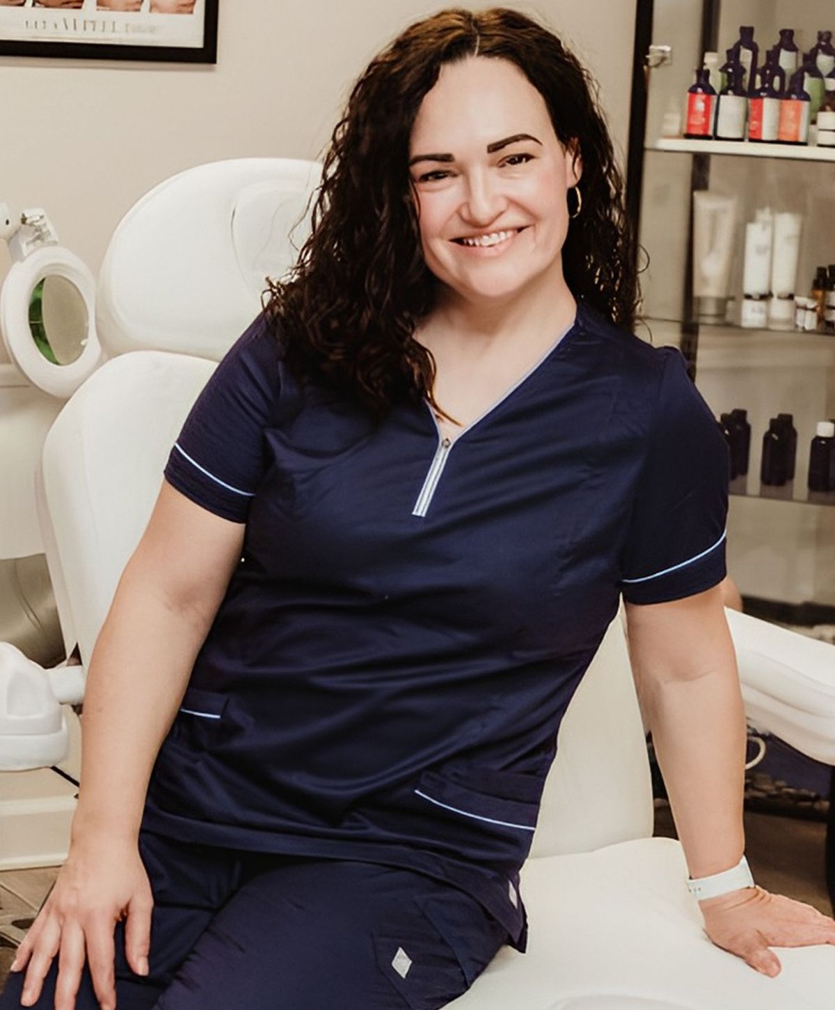 Smiling woman in medical uniform, seated in clinic.