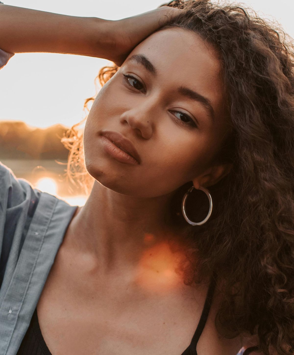 Young woman with curly hair outdoors at sunset.