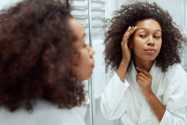Woman applying skincare in front of mirror.