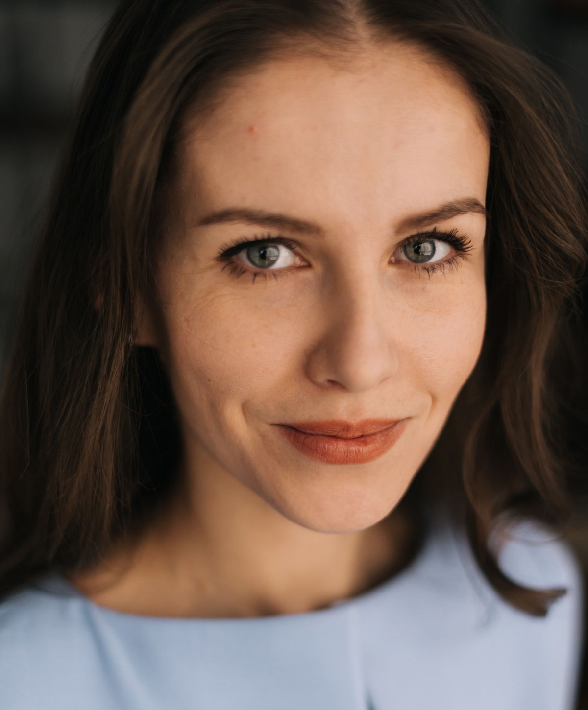 Woman smiling in light blue top with soft lighting.