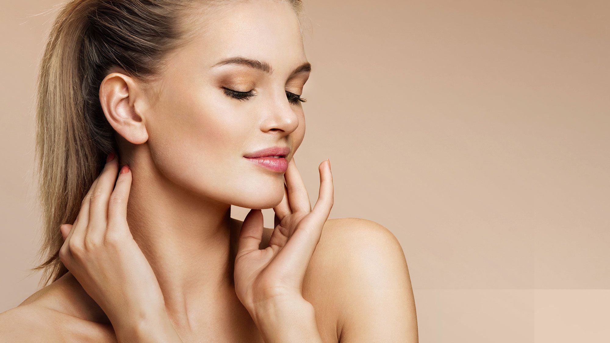Woman gently touching her face, neutral background.