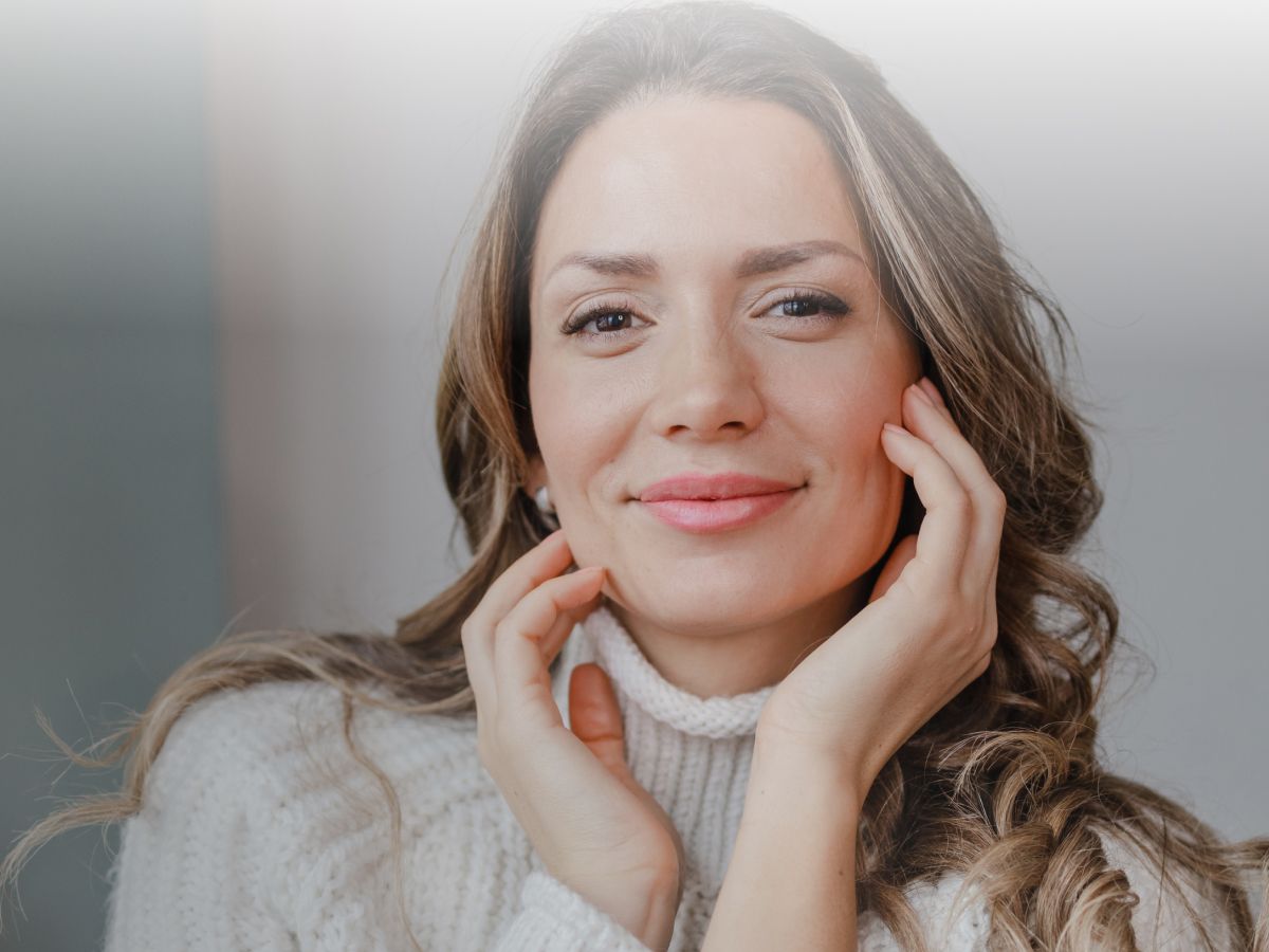 Smiling woman in cozy sweater, hands on face.