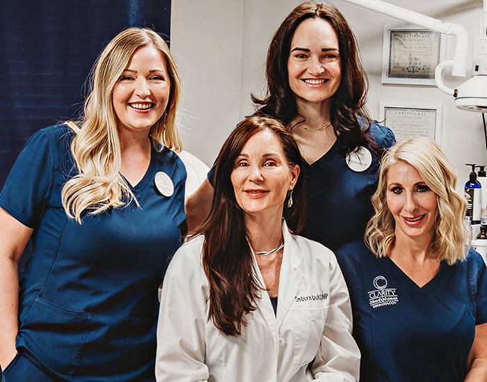 Four women in medical attire smiling together.