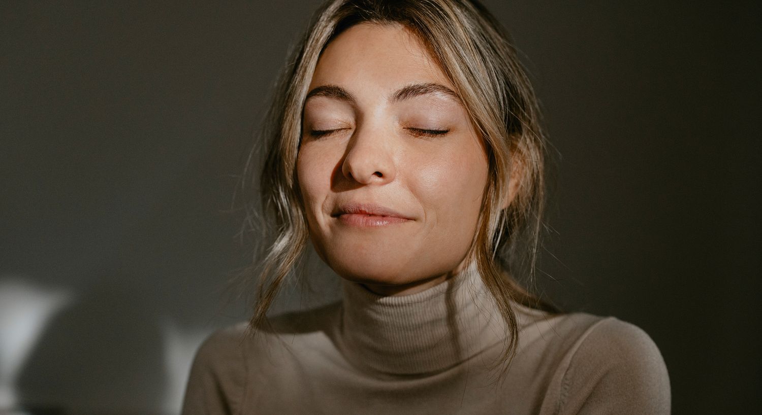 Woman with closed eyes, smiling softly in sunlight.