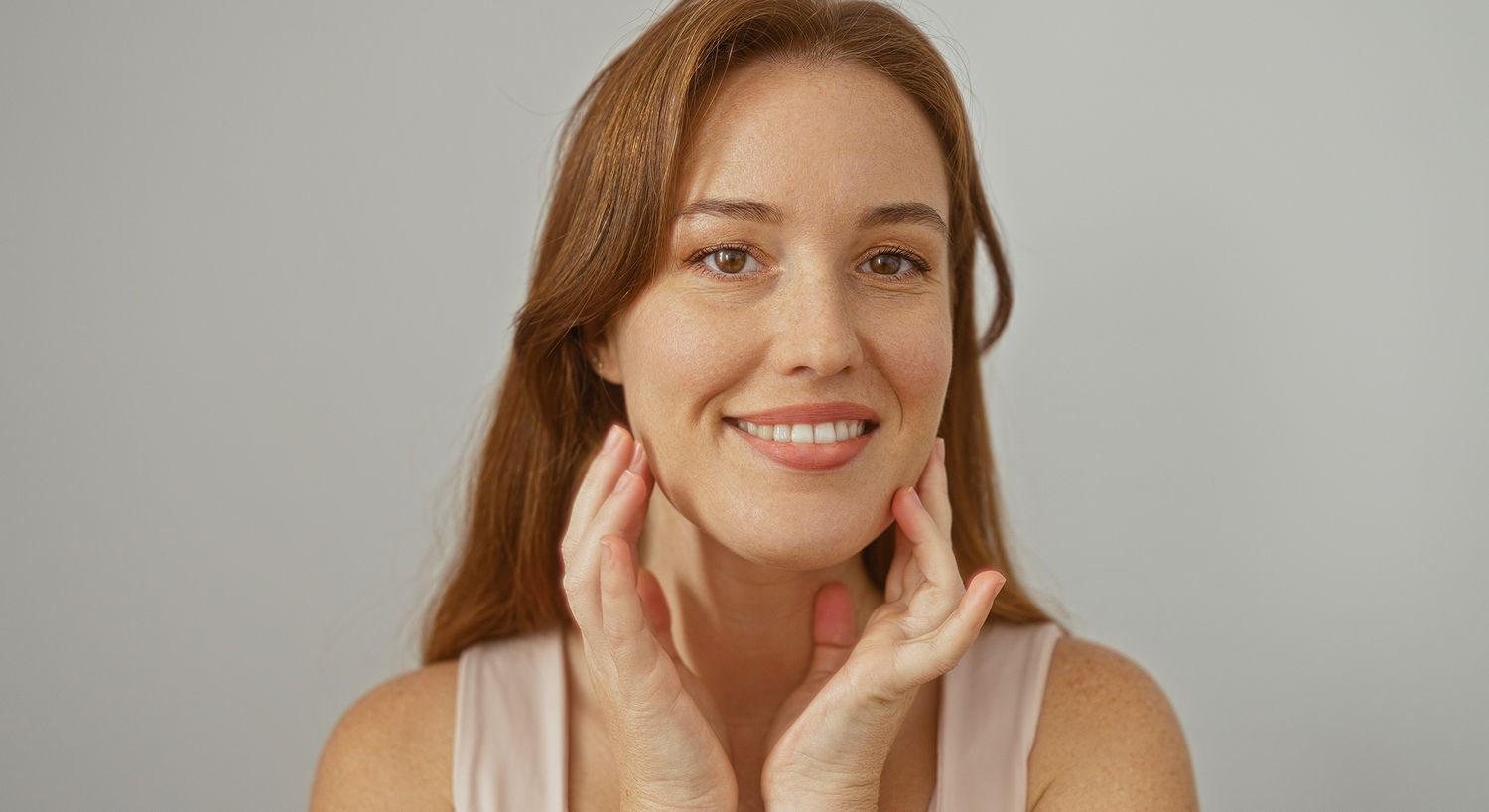 Smiling woman showcasing skincare routine with hands.